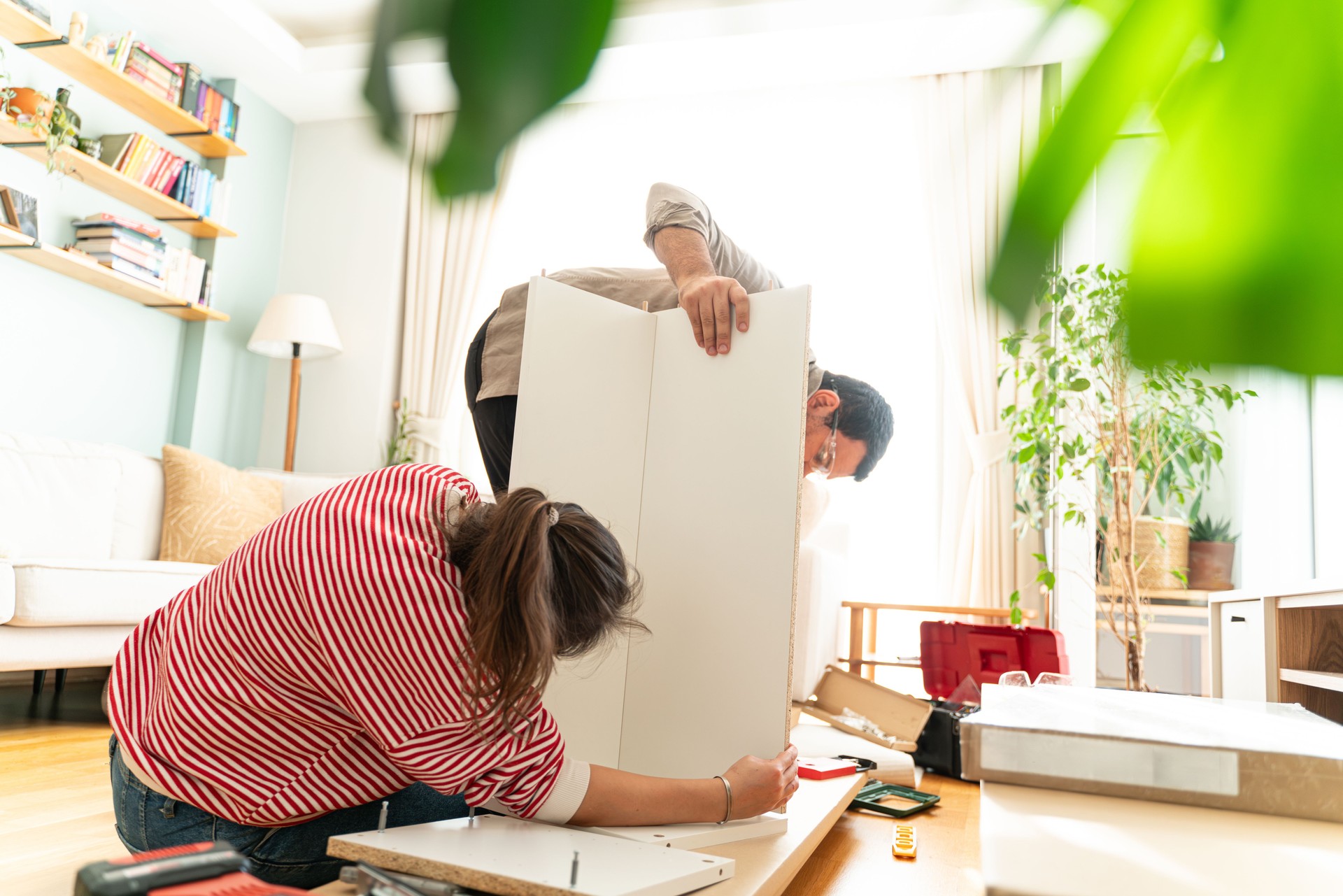 Happy Couple Assembles Furniture as a Team, Girl Reads Instructions and Boy Tightens Screw with a Drill. Moving into New Apartment, Couple Assemble Shelf.